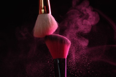 Photo of Makeup brushes with pink eye shadow on black background, closeup