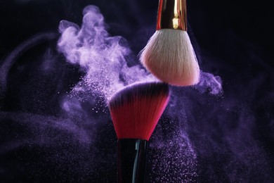 Photo of Makeup brushes with purple eye shadow on black background, closeup