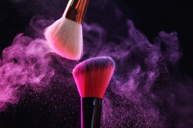 Photo of Makeup brushes with colorful eye shadows in neon lights on black background, closeup