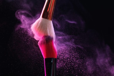 Photo of Makeup brushes with colorful eye shadows in neon lights on black background, closeup