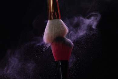 Photo of Makeup brushes with purple eye shadow on black background, closeup