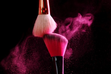 Photo of Makeup brushes with pink eye shadow on black background, closeup