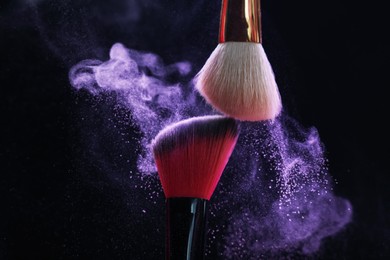 Photo of Makeup brushes with purple eye shadow on black background, closeup