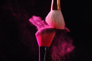 Photo of Makeup brushes with pink eye shadow on black background, closeup
