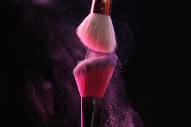 Photo of Makeup brushes with pink eye shadow on black background, closeup