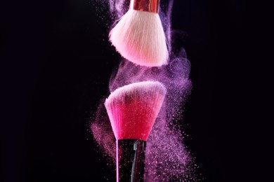 Photo of Makeup brushes with color eye shadow on black background, closeup
