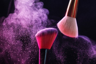 Photo of Makeup brushes with color eye shadow on black background, closeup