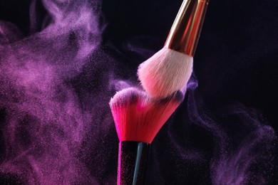 Photo of Makeup brushes with color eye shadow on black background, closeup