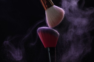 Photo of Makeup brushes with purple eye shadow on black background, closeup