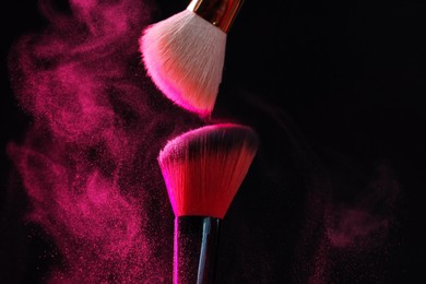 Photo of Makeup brushes with pink eye shadow on black background, closeup