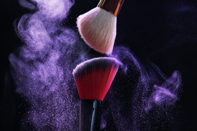 Photo of Makeup brushes with purple eye shadow on black background, closeup