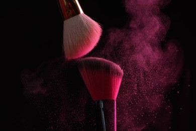 Photo of Makeup brushes with pink eye shadow on black background, closeup