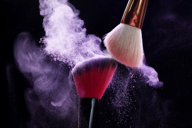Photo of Makeup brushes with purple eye shadow on black background, closeup