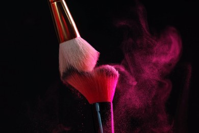 Photo of Makeup brushes with pink eye shadow on black background, closeup