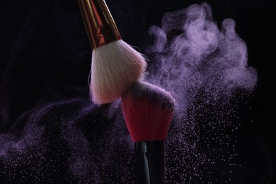 Photo of Makeup brushes with purple eye shadow on black background, closeup