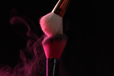 Photo of Makeup brushes with pink eye shadow on black background, closeup