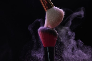 Photo of Makeup brushes with purple eye shadow on black background, closeup