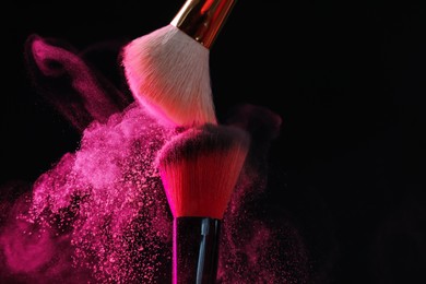 Photo of Makeup brushes with pink eye shadow on black background, closeup
