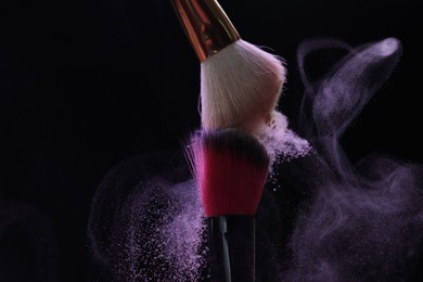 Photo of Makeup brushes with purple eye shadow on black background, closeup