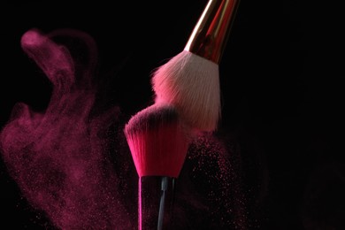 Photo of Makeup brushes with pink eye shadow on black background, closeup