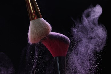 Photo of Makeup brushes with purple eye shadow on black background, closeup