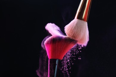 Photo of Makeup brushes with colorful eye shadows on black background, closeup