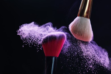 Photo of Makeup brushes with purple eye shadow on black background, closeup