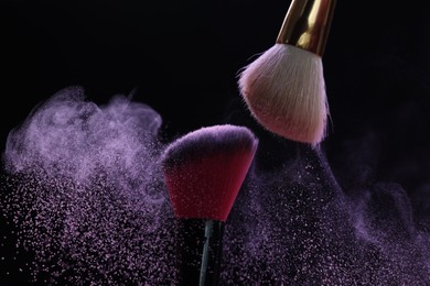Photo of Makeup brushes with purple eye shadow on black background, closeup