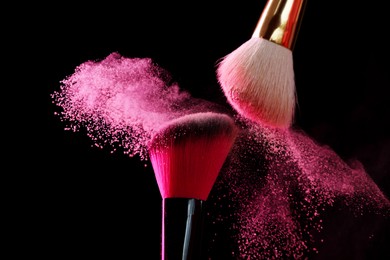 Photo of Makeup brushes with pink eye shadow on black background, closeup