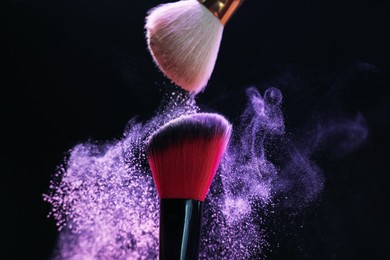 Photo of Makeup brushes with purple eye shadow on black background, closeup