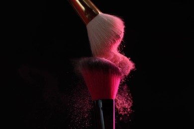 Photo of Makeup brushes with pink eye shadow on black background, closeup