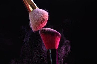 Photo of Makeup brushes with pink eye shadow on black background, closeup