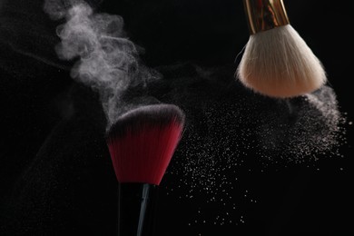 Photo of Makeup brushes with cosmetic powder on black background, closeup