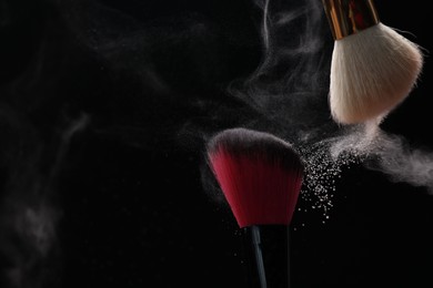 Photo of Makeup brushes with cosmetic powder on black background, closeup. Space for text