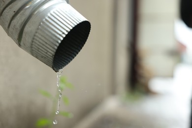 Photo of Water dripping from drain pipe outdoors, closeup. Space for text