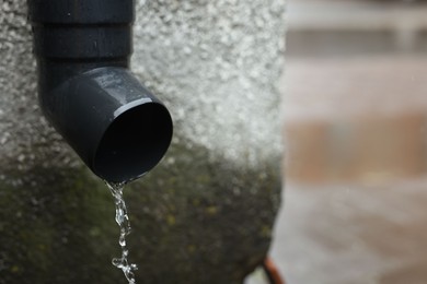 Photo of Water dripping from drain pipe outdoors, closeup. Space for text