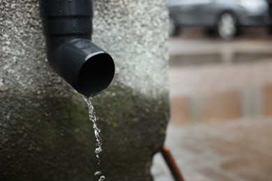 Photo of Water dripping from drain pipe outdoors, closeup. Space for text