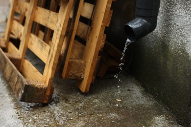 Photo of Water flowing from drain pipe and wooden planks outdoors