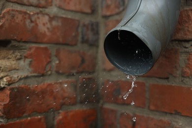 Photo of Water dripping from drain pipe outdoors, closeup. Space for text