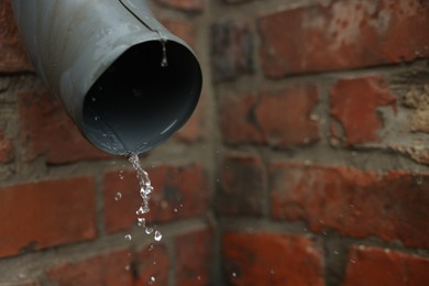 Photo of Water dripping from drain pipe outdoors, closeup. Space for text