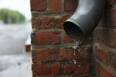 Photo of Water dripping from drain pipe outdoors, closeup