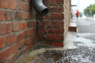 Photo of Water dripping from drain pipe outdoors, space for text