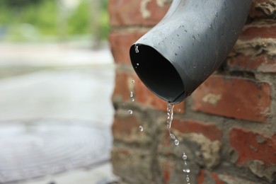Photo of Water dripping from drain pipe outdoors, closeup. Space for text