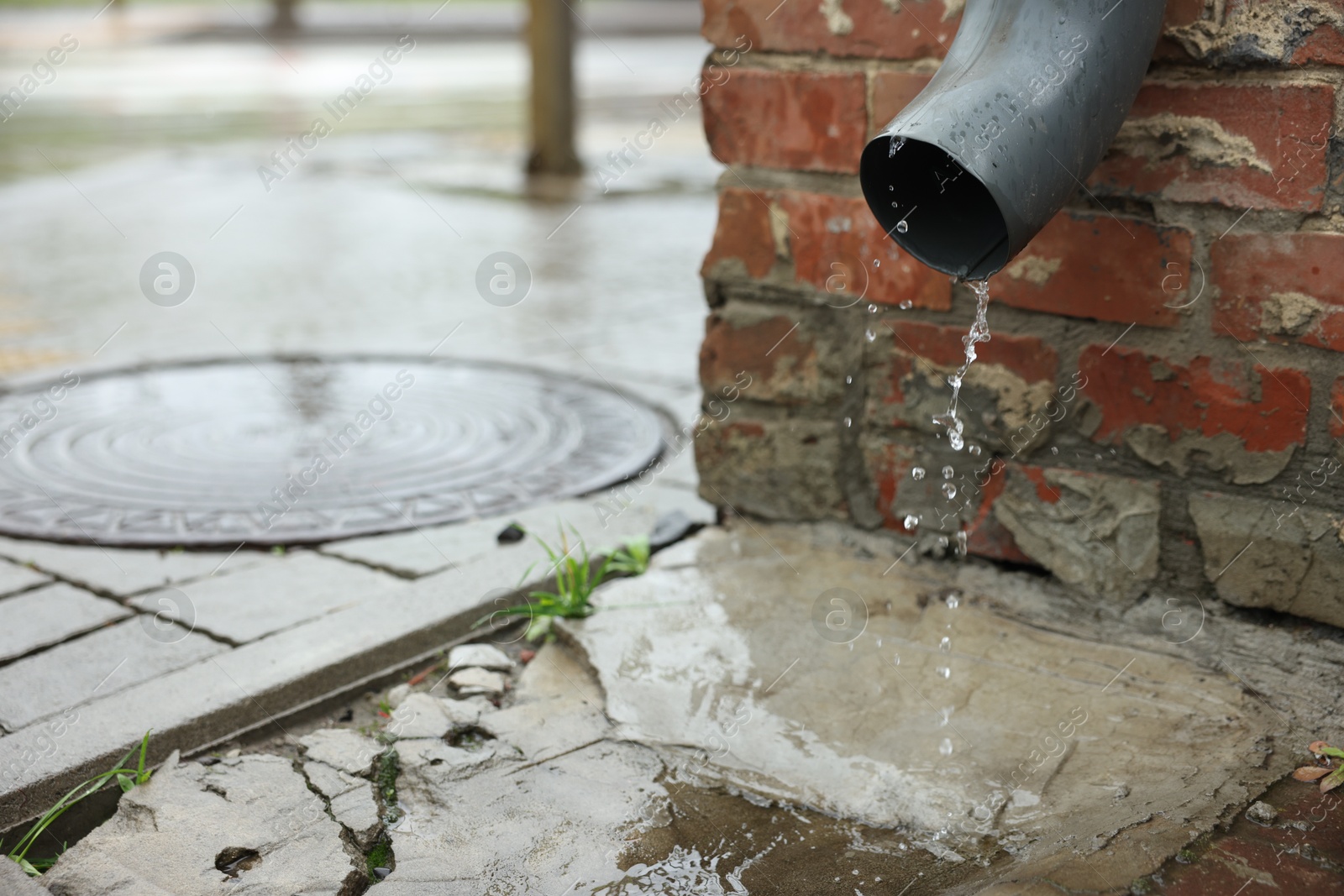 Water dripping from drain pipe outdoors, space for text Photo of Water dripping from drain pipe outdoors, space for text