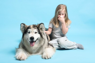 Photo of Girl suffering from allergy with her dog on light blue background