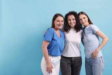 Photo of Three friends hugging on light blue background, space for text