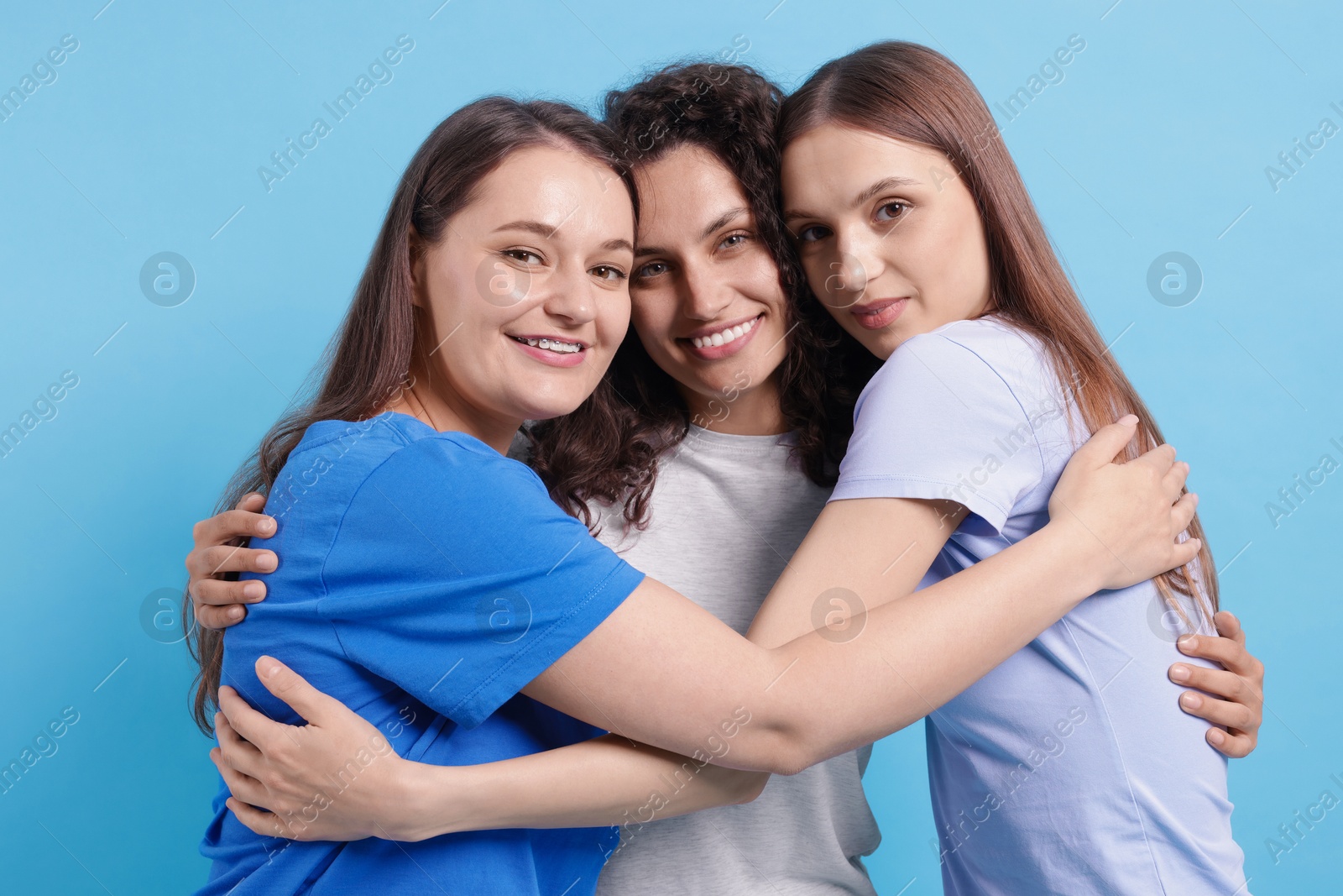 Photo of Three friends hugging on light blue background