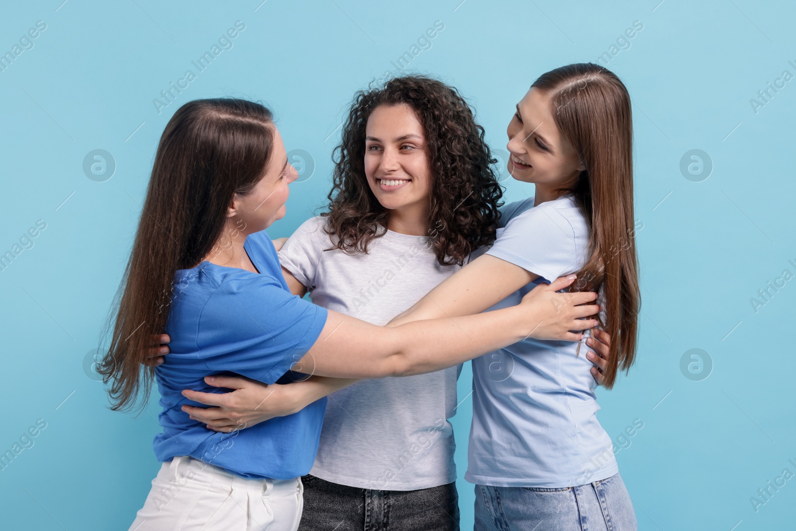 Three friends hugging on light blue background Photo of Three friends hugging on light blue background