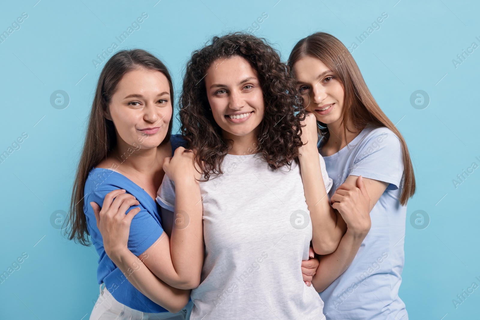 Three friends hugging on light blue background Photo of Three friends hugging on light blue background