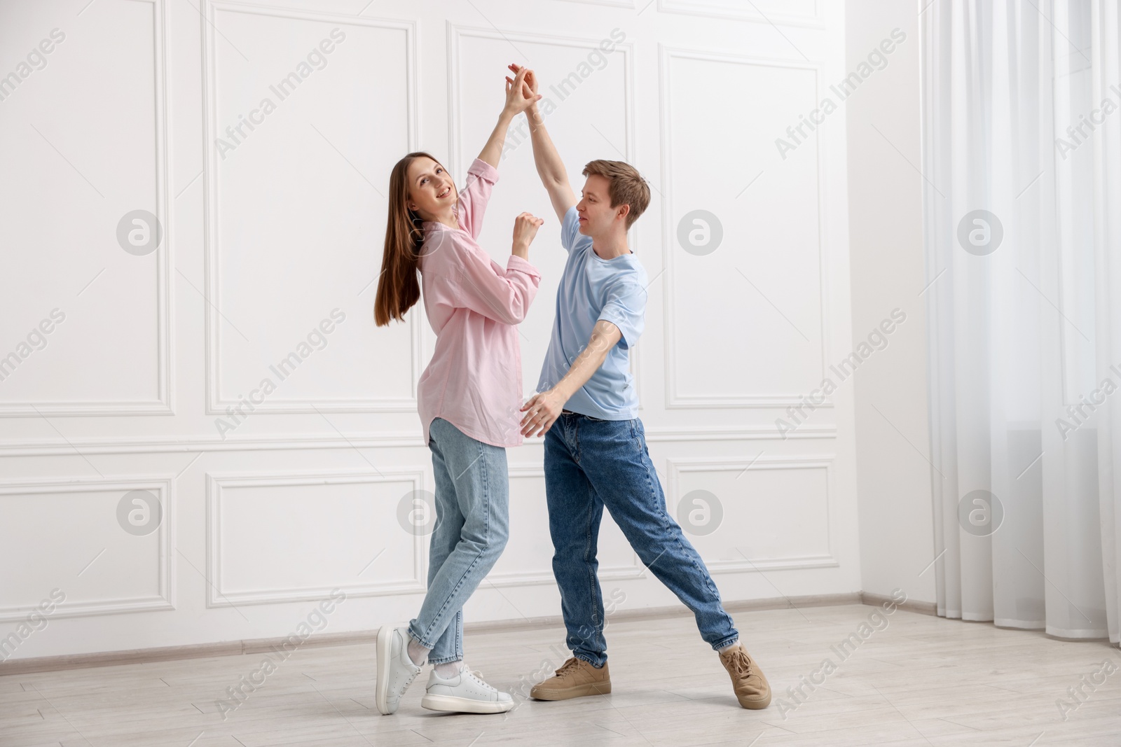 Happy couple dancing together near white wall at home Photo of Happy couple dancing together near white wall at home